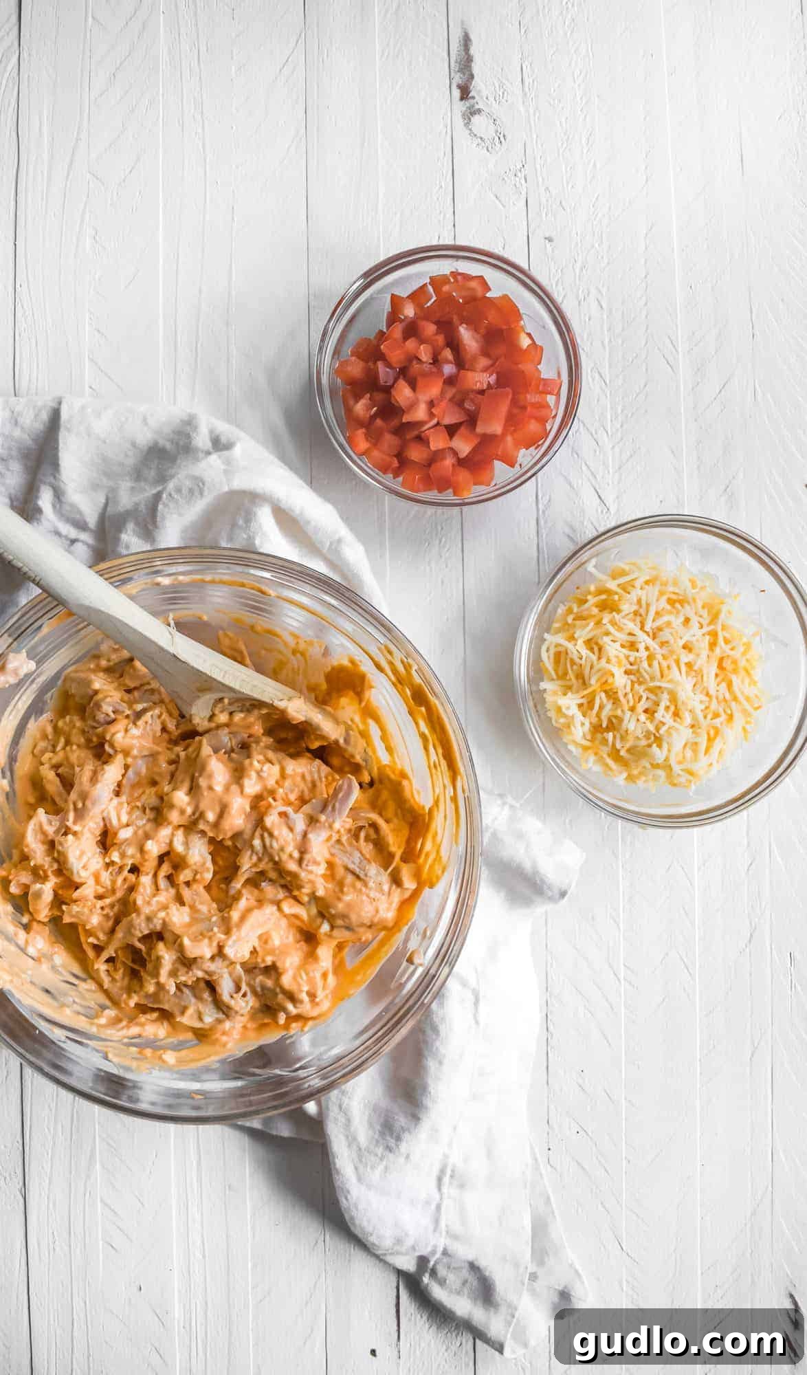 A vibrant flat lay of all the fresh and prepared ingredients needed for making Buffalo Chicken Nachos, including bowls of shredded chicken, buffalo sauce, various cheeses, and expertly chopped carrots and celery.