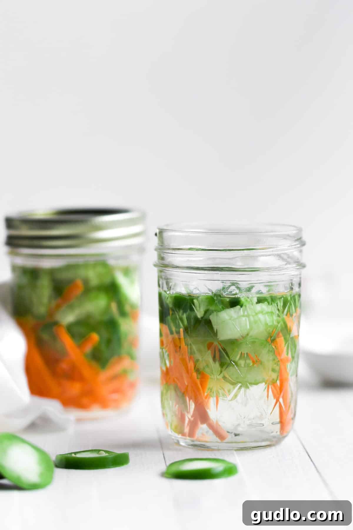 Two clear glass mason jars showcasing vibrant, freshly prepared quick-pickled carrots, celery, and jalapeños, glistening in their flavorful brine, highlighting their crisp texture and bright colors.