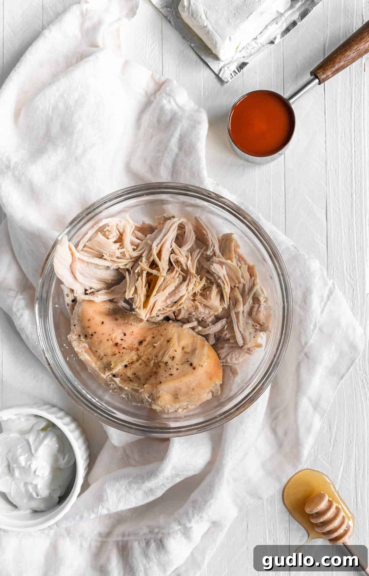 A large bowl brimming with perfectly shredded chicken, generously coated in a rich and creamy buffalo sauce, ready to be layered onto crispy tortilla chips for the ultimate nacho experience.