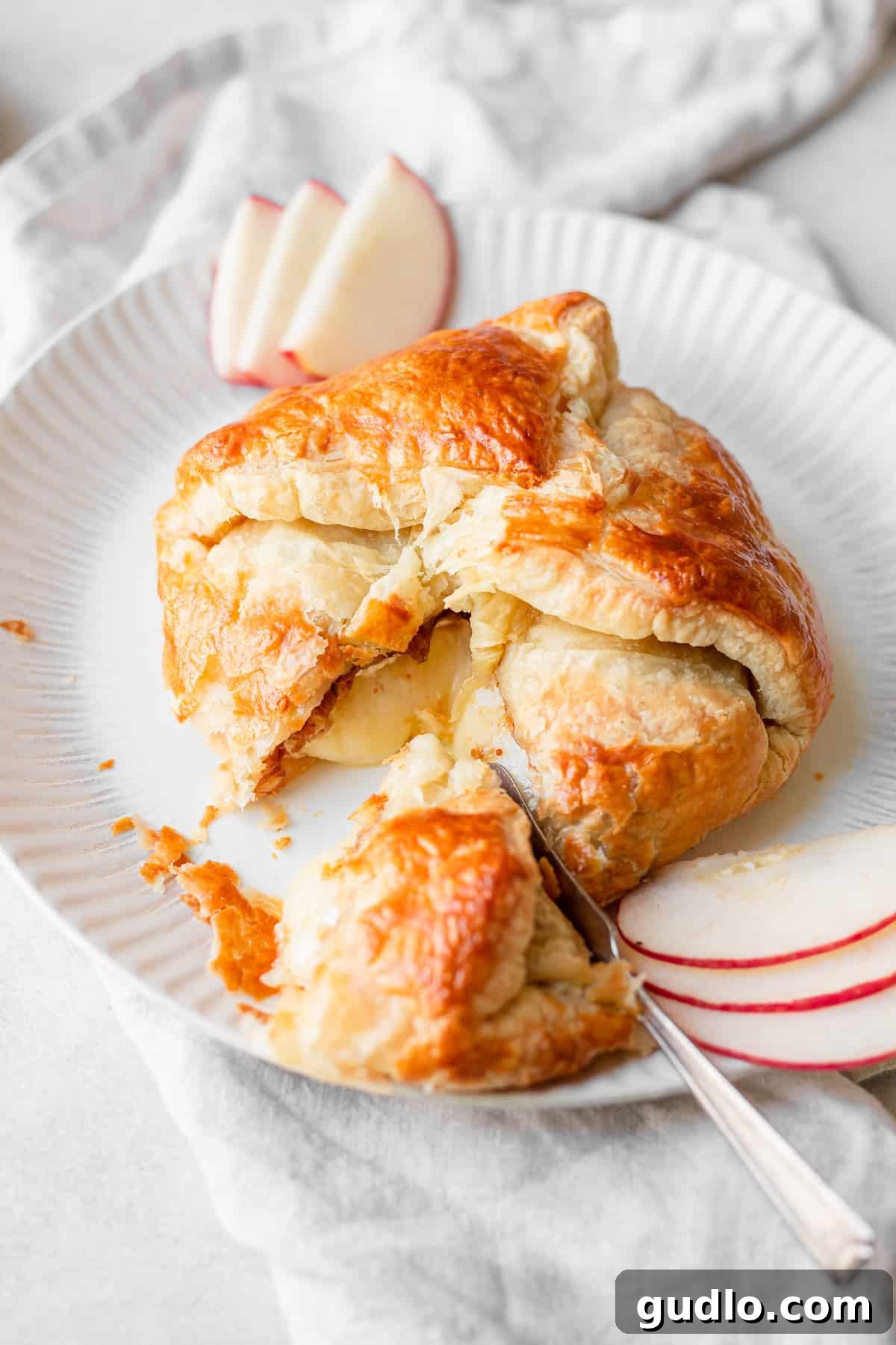 baked brie with fig jam on plate, showcasing its golden-brown puff pastry and oozing cheese.