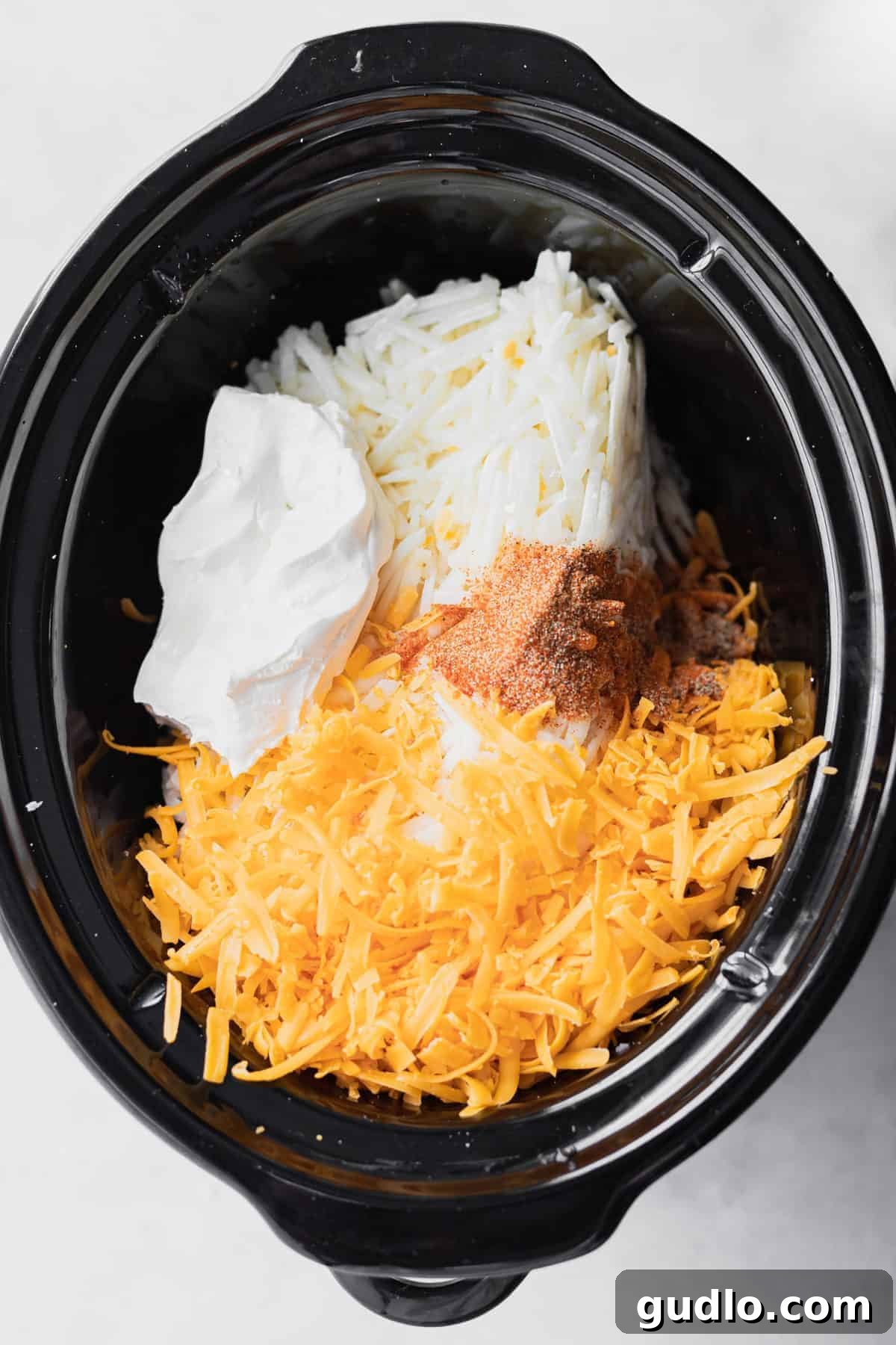 A Crockpot Cheesy Potatoes recipe is a recipe that everyone needs in their back pocket. They're the perfect side to serve at any holiday or gathering because EVERYONE likes them. All the essential ingredients for crockpot cheesy potatoes laid out next to a slow cooker, ready for preparation.