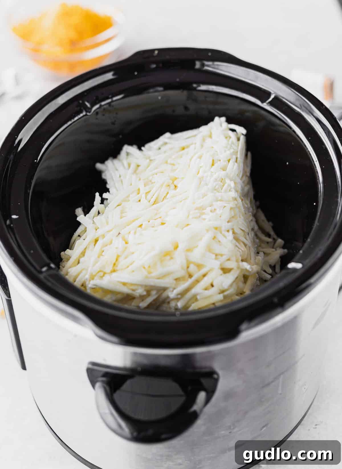 Make these crockpot cheesy potatoes with real potatoes in no time using your slow cooker and just 5 main ingredients! A close-up shot of ingredients for crockpot cheesy potatoes mixed together in a slow cooker before cooking.