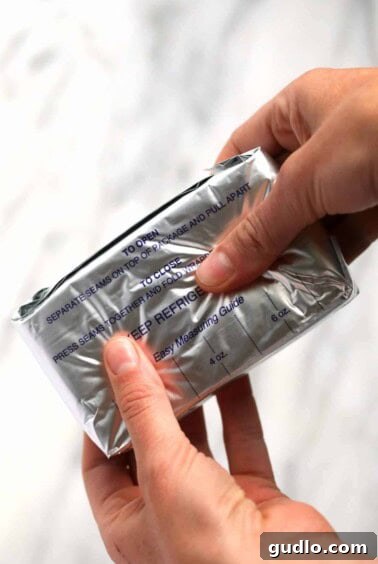 Hands massaging cream cheese through its wrapper to soften it.