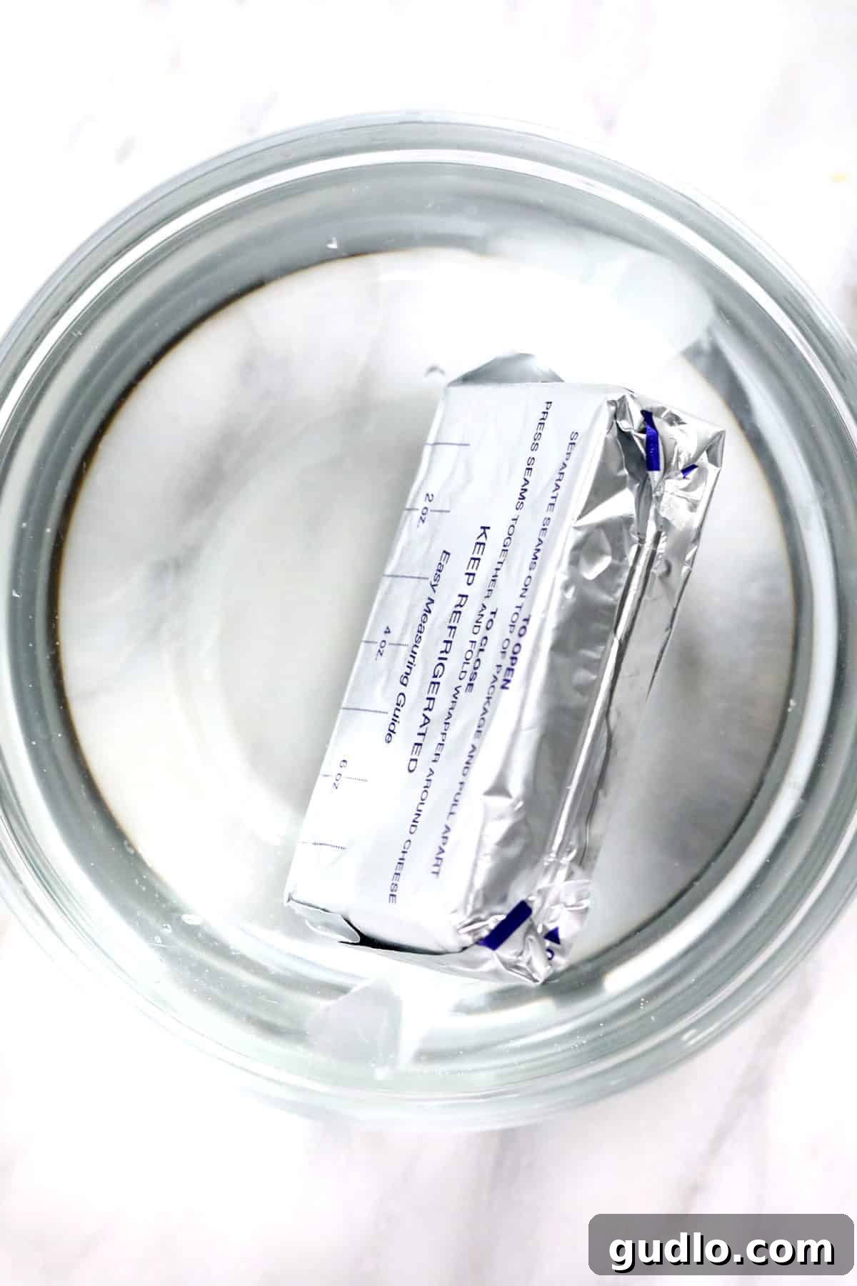 Wrapped cream cheese submerged in a bowl of warm water.