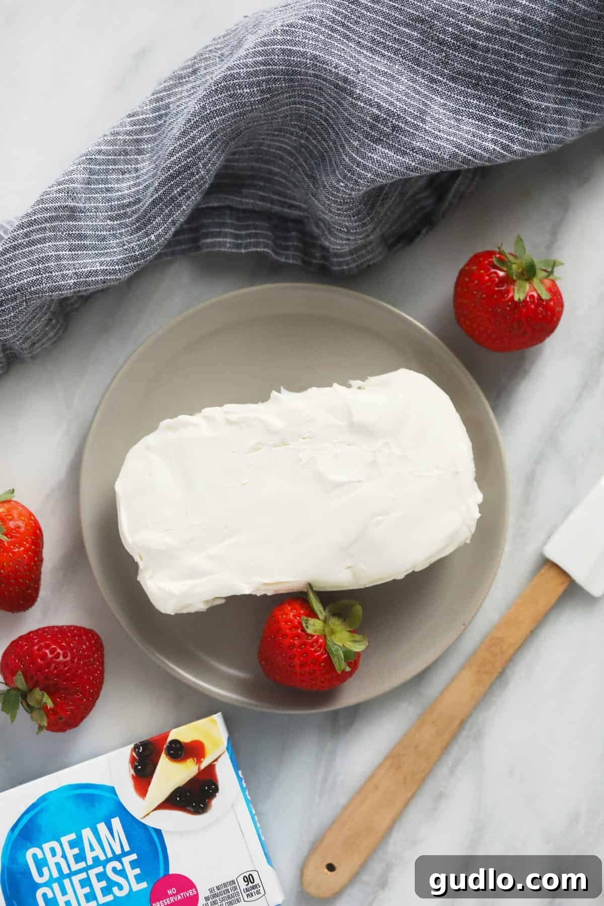 Unwrapped cream cheese on a microwave-safe plate, ready for softening.