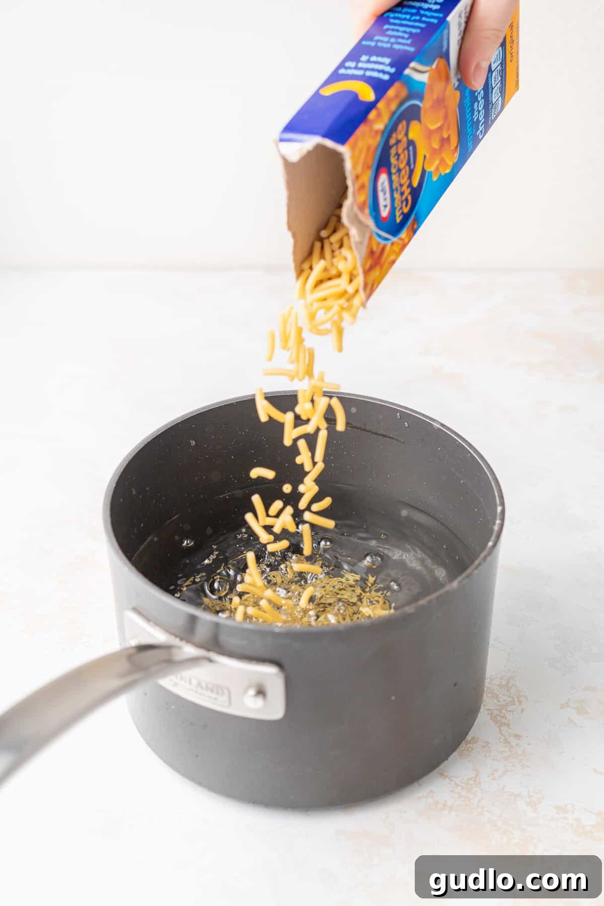 Next-Level Boxed Mac and Cheese Hacks 3 Pouring macaroni noodles into a saucepan, preparing for the sauce.