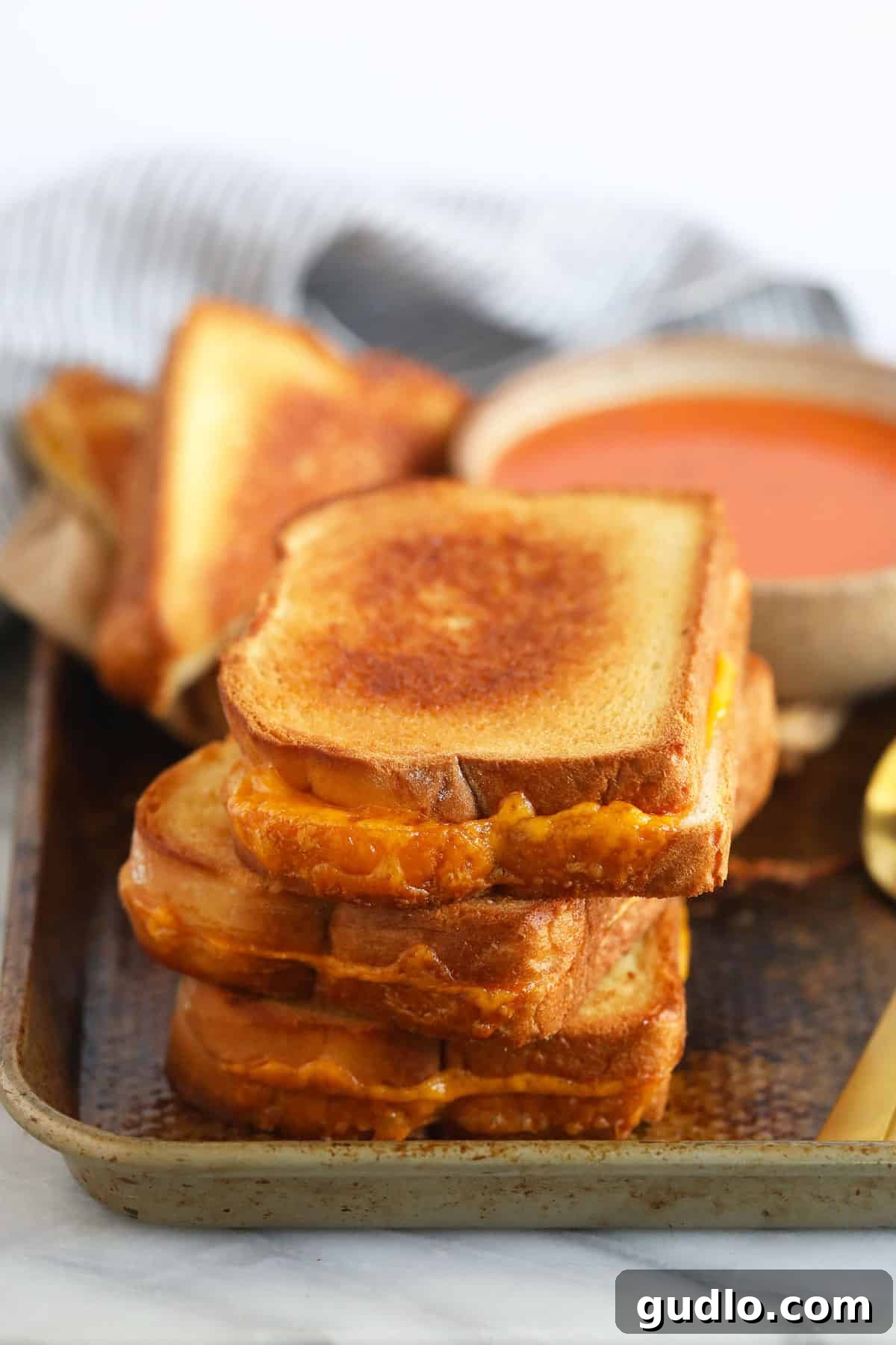 Serve delicious sheet pan grilled cheese to a group with ease! Golden brown sheet pan grilled cheese sandwiches served next to a steaming bowl of rich tomato soup, ready to be enjoyed by a group.