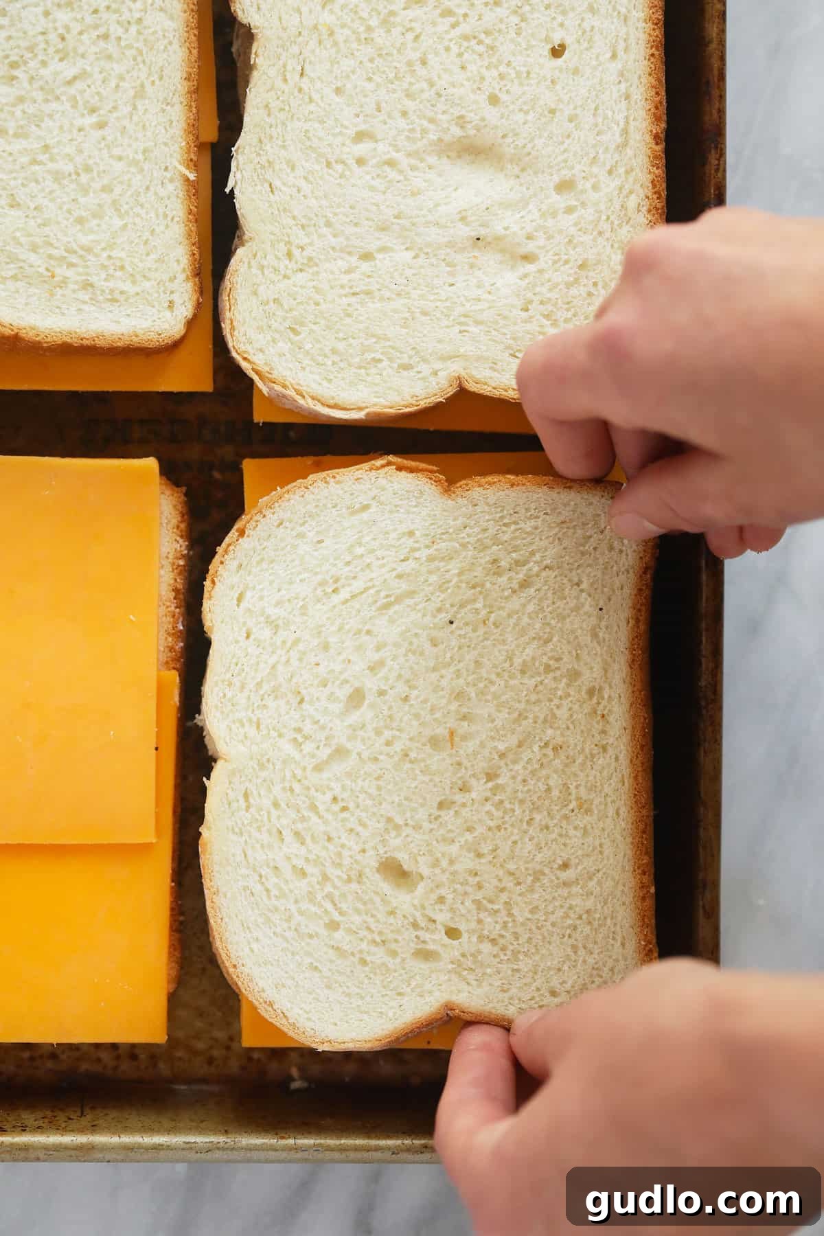Assembled grilled cheese sandwiches on a baking sheet, ready for the oven. Several sheet pan grilled cheese sandwiches laid out on a baking sheet, buttered and ready to be put into the oven to bake until golden and gooey.
