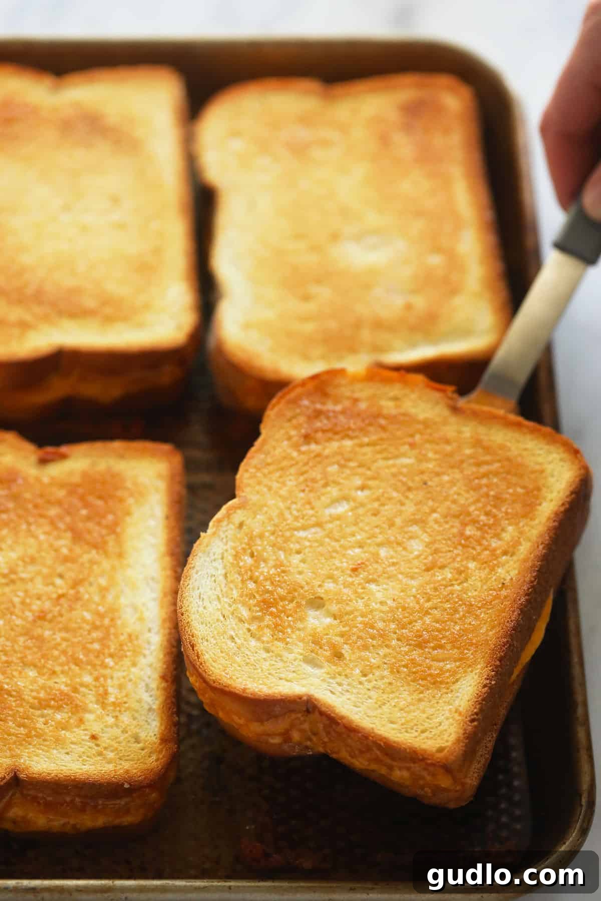 Golden brown sheet pan grilled cheese perfection. Perfectly baked sheet pan grilled cheese sandwiches, golden brown and crispy, with melted cheese oozing slightly, stacked on a cutting board.