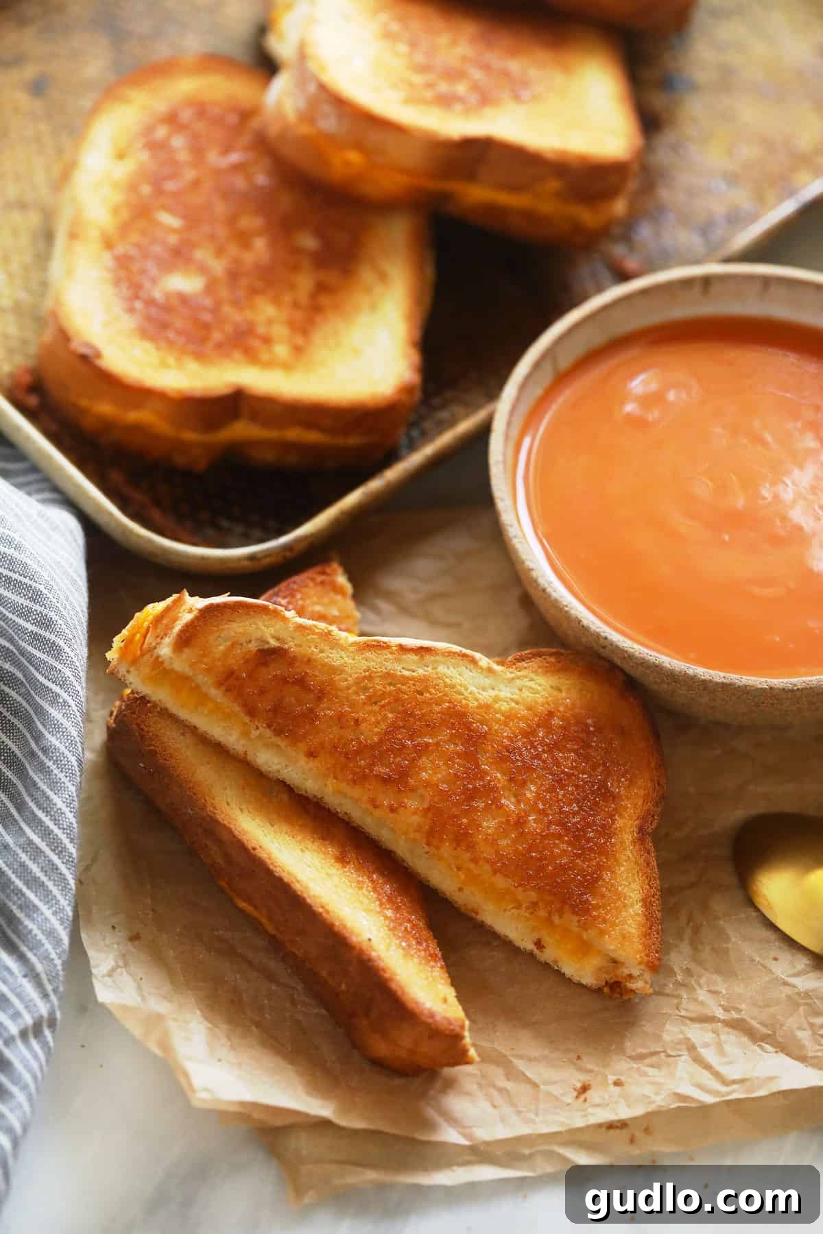 Sheet pan grilled cheese and tomato soup, a perfect pairing. Two freshly baked sheet pan grilled cheese sandwiches, perfectly sliced diagonally, served alongside a bowl of rich tomato soup, steam rising enticingly.