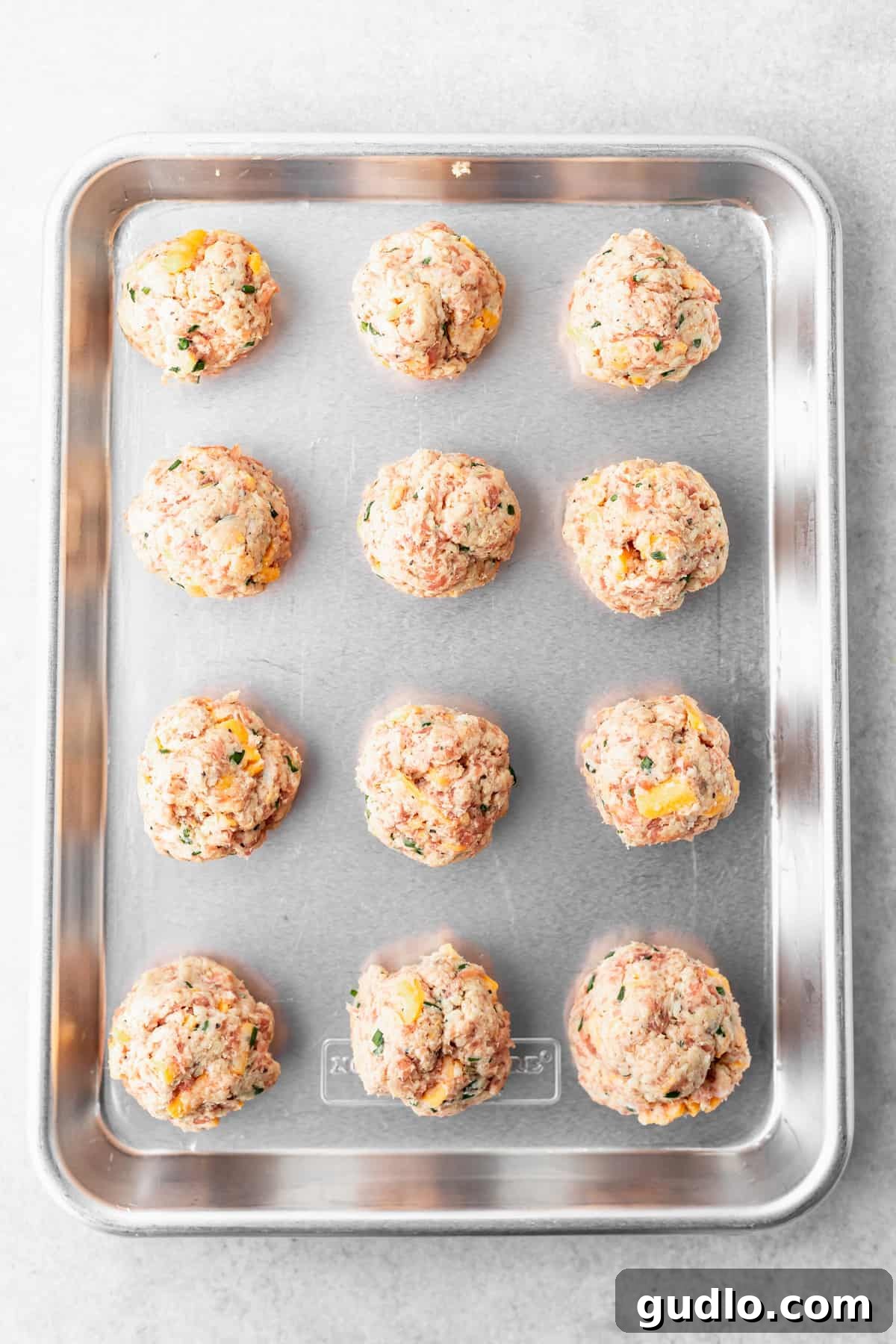 These Cream Cheese Sausage Balls make a fantastic appetizer for any occasion! Dip them in a perfectly zesty creamy garlic sauce, and enjoy! raw cream cheese sausage balls on a baking tray ready to be cooked