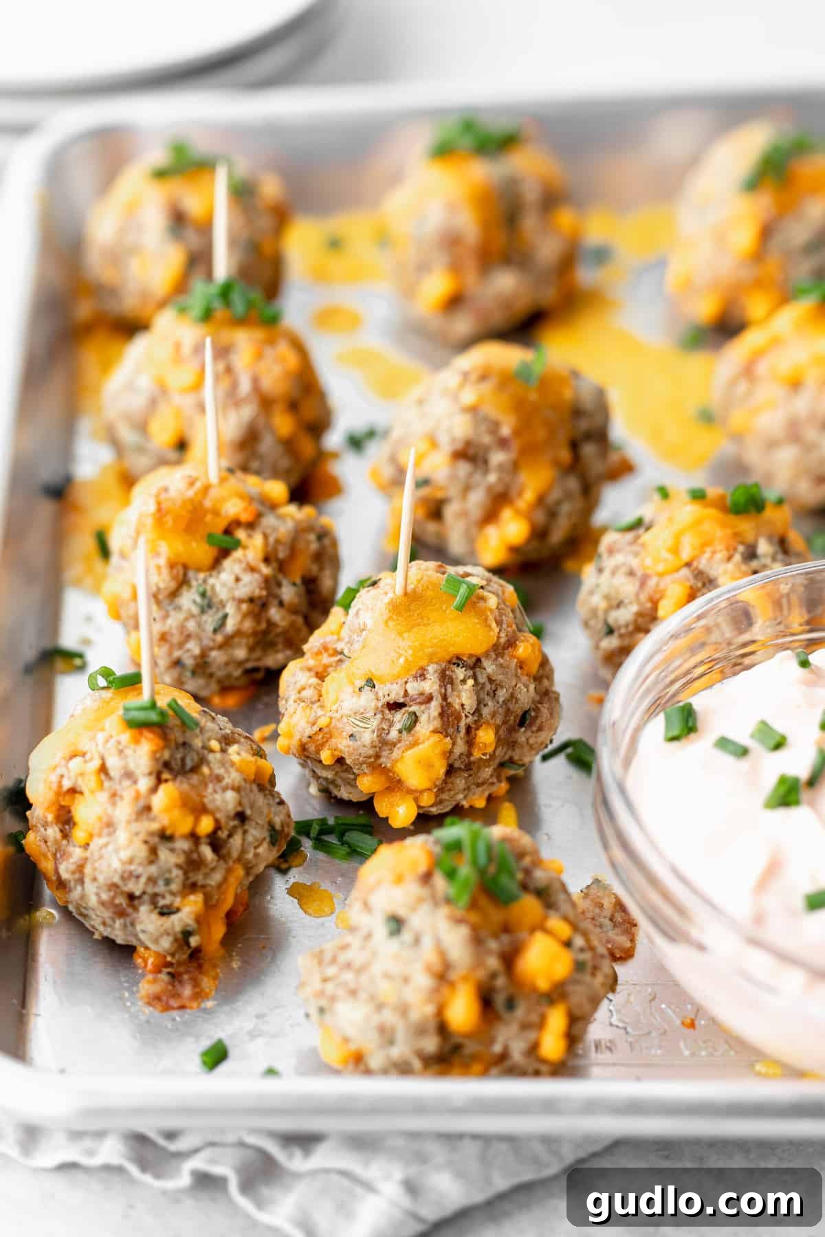 These Cream Cheese Sausage Balls make a fantastic appetizer for any occasion! Dip them in a perfectly zesty creamy garlic sauce, and enjoy! cream cheese sausage balls on a baking tray with toothpicks, ready to be dipped into garlic sauce