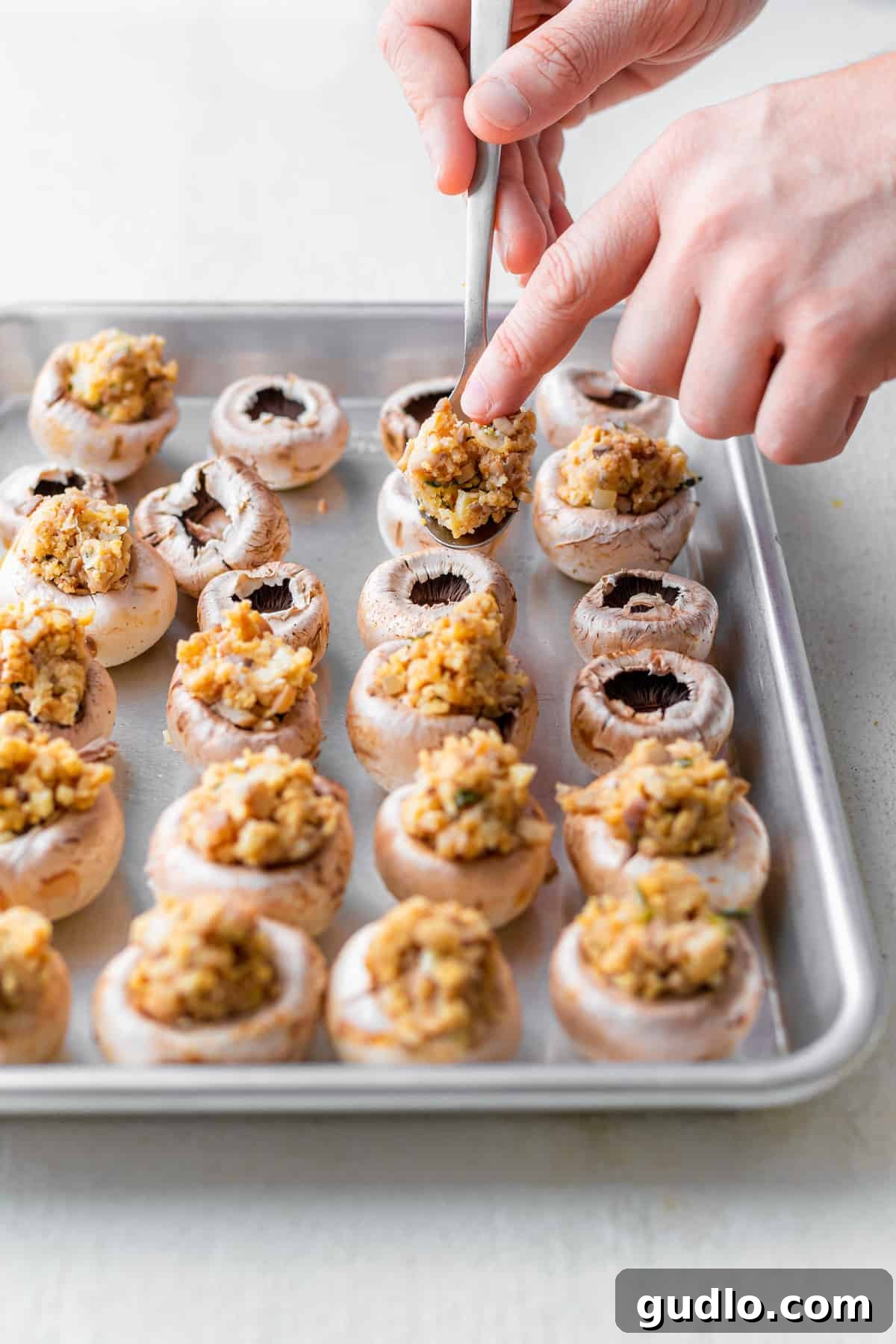 Hands carefully filling mushroom caps with a rich cream cheese mixture, preparing them for baking.