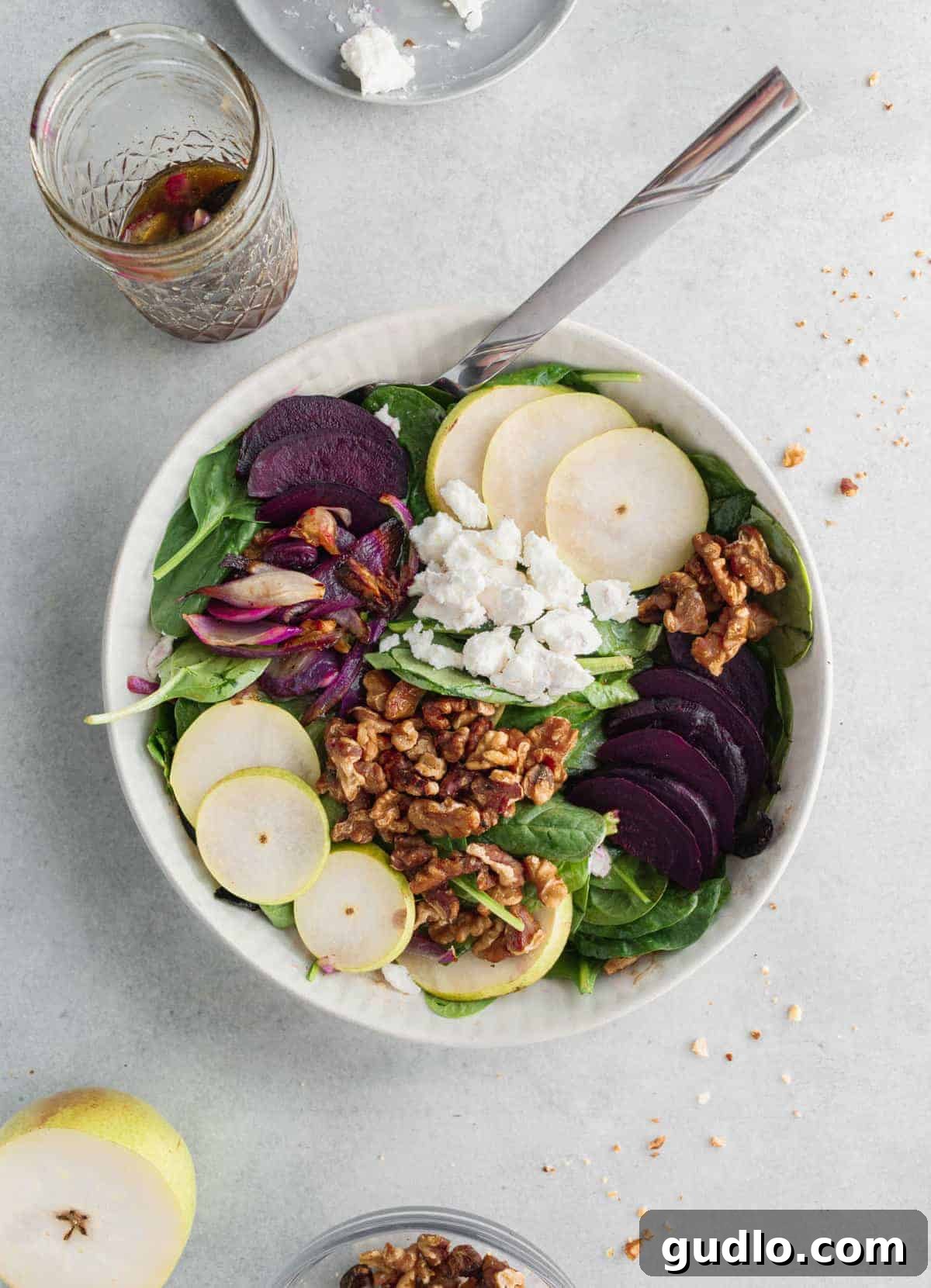 Roasted Beet and Creamy Goat Cheese Salad 2 A large bowl filled with a vibrant beet goat cheese salad, featuring roasted beets, goat cheese crumbles, sliced pears, and candied walnuts over a bed of spinach.