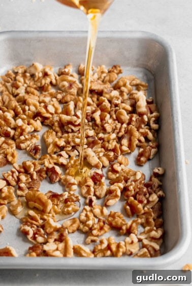 Walnuts drizzled with maple syrup on a baking sheet, ready for candying.