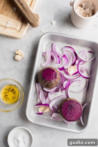 Beets, purple onion, and garlic cloves roasting in a baking dish.