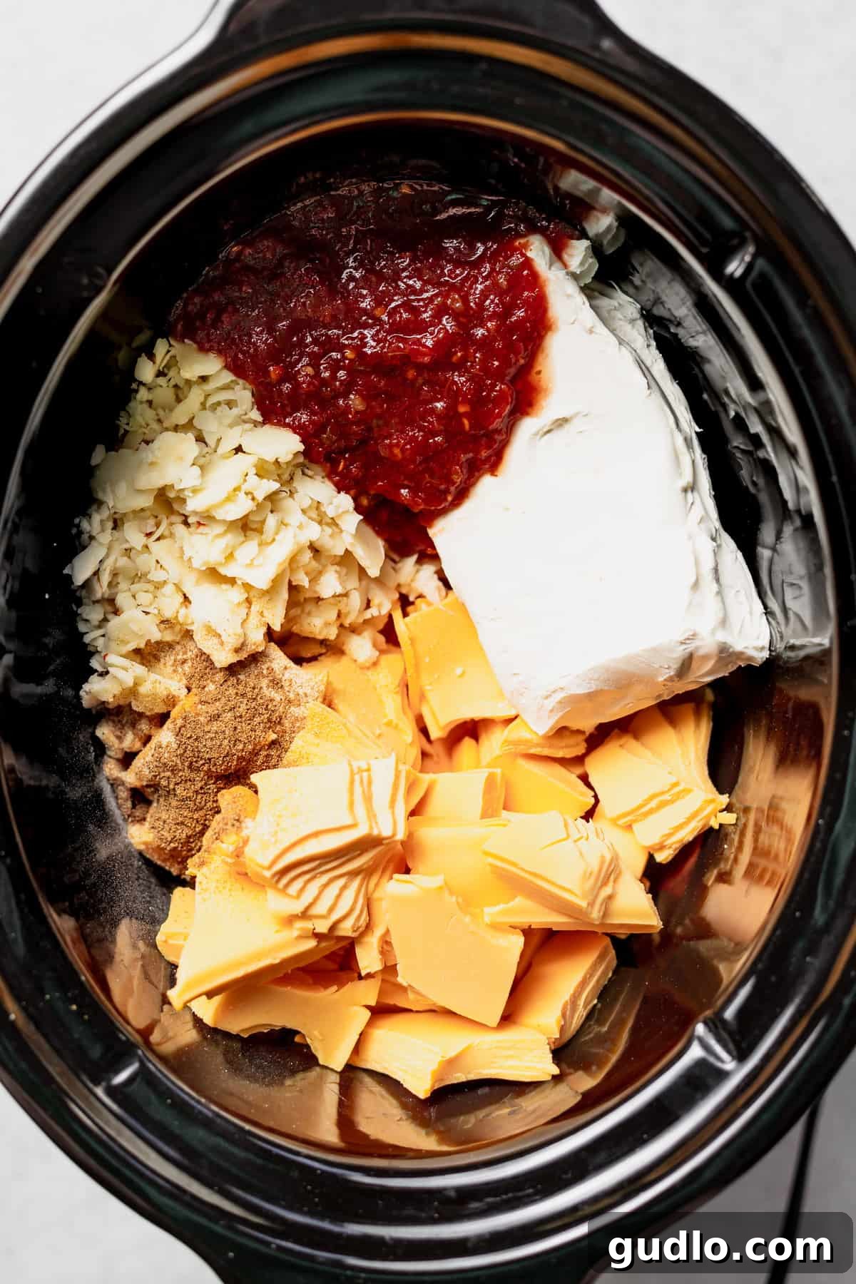 Ingredients for Slow Cooker Queso Dip A slow cooker filled with various cheese cubes, salsa, and milk, ready to be melted into a smooth queso dip.