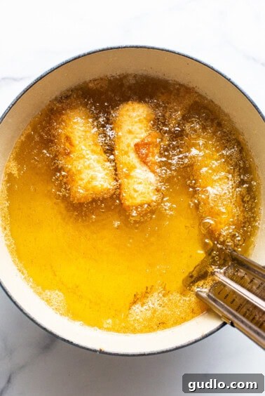 Reuben egg rolls frying in a pot of hot oil.