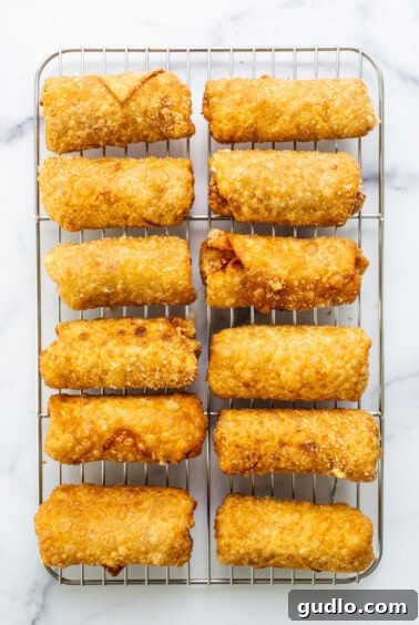 Freshly fried Reuben egg rolls on a cooling rack with dipping sauce.