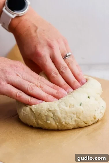 Two hands shaping a round piece of dough on a sheet of parchment paper.