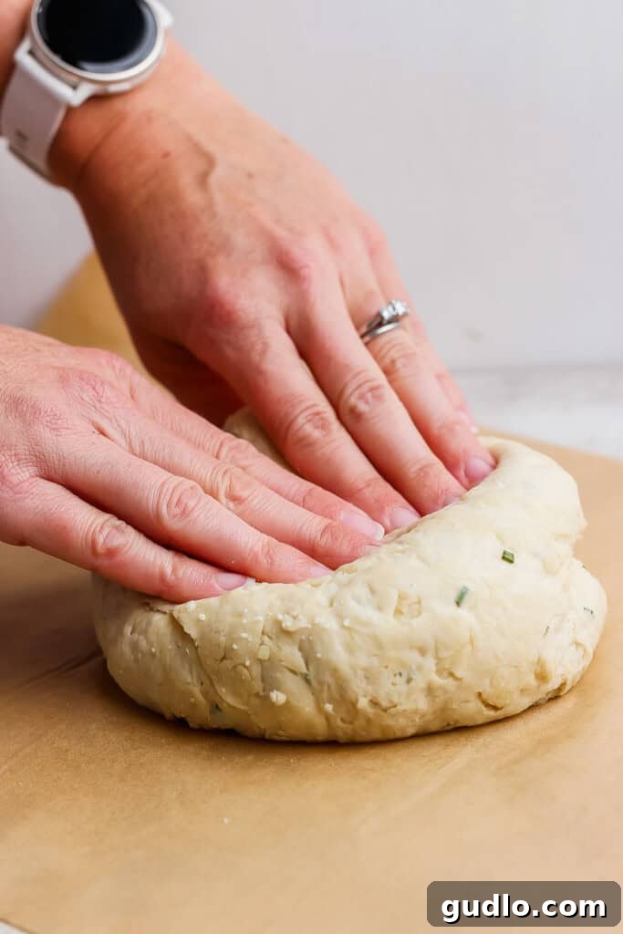 Two hands shaping a round piece of dough on a sheet of parchment paper.