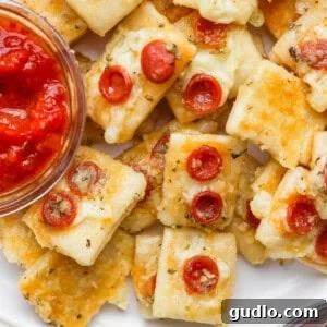 Close-up of mini cheese and pepperoni pizza bites on a plate with a small bowl of marinara dipping sauce.