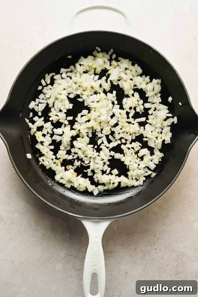 Diced onions being sautéed in a black skillet to build the flavor base for the dip.
