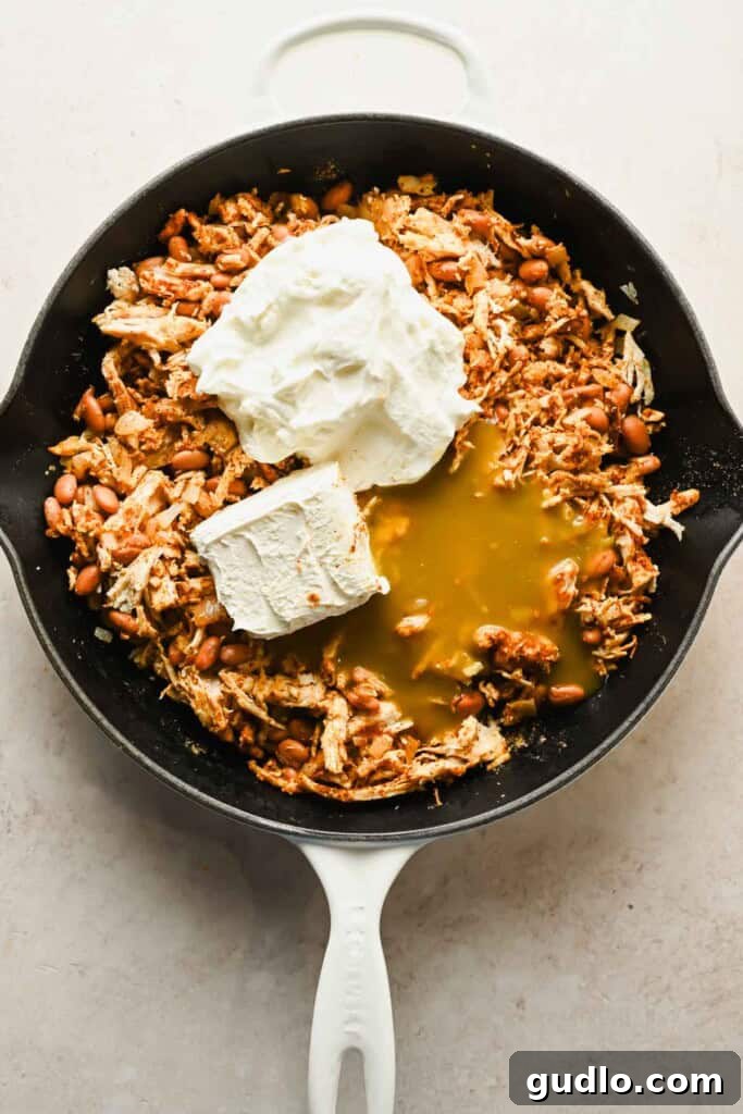 The skillet showing all ingredients like chicken, beans, and cream cheese before being mixed together.