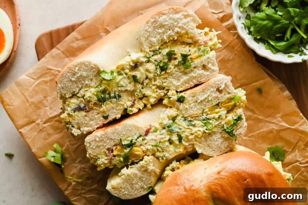 A perfectly assembled Street Corn Chopped Bagel, sliced in half to show the vibrant, chunky filling of corn, bacon, eggs, and herbs on a wooden board.