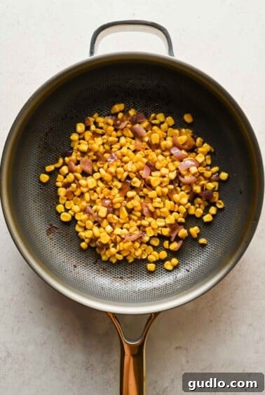 Charred corn kernels and minced red onion sauteing in a skillet with bacon fat.