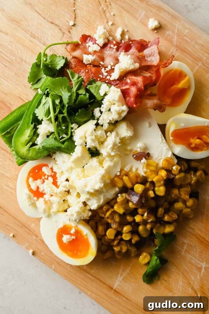All the fresh ingredients for the Street Corn Chopped Bagel laid out on a wooden board: soft-boiled eggs, charred corn, crispy bacon, jalapeño, cilantro, and cotija cheese.