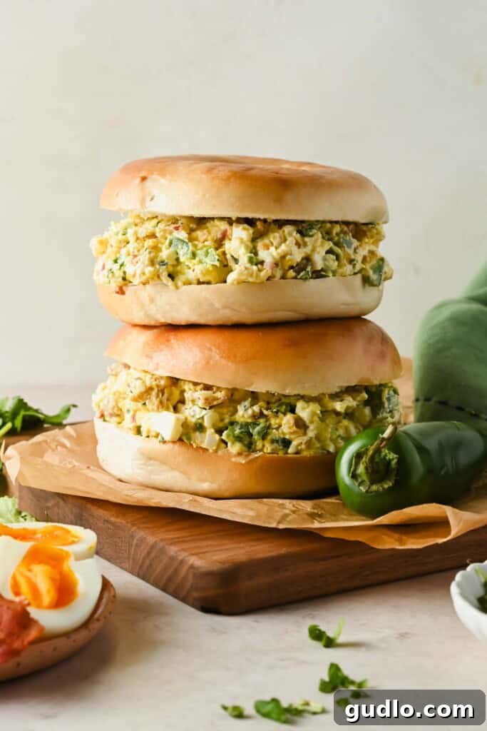 Two stacked halves of a street corn chopped bagel sandwich on a wooden board, showing the thick layer of creamy, chunky filling.