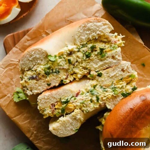 A close up shot of a perfectly toasted bagel filled with a generous amount of street corn chopped egg salad, sitting on parchment paper.