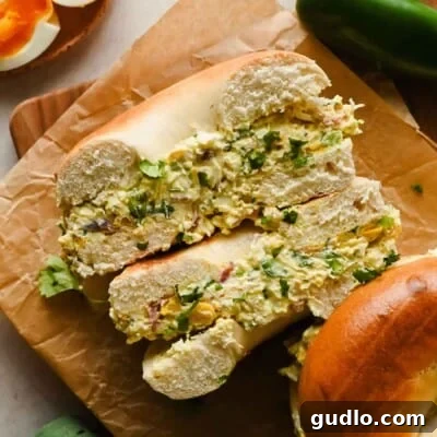 A bagel sliced in half and filled with a chunky egg salad, garnished with chopped herbs, sits on brown parchment paper.