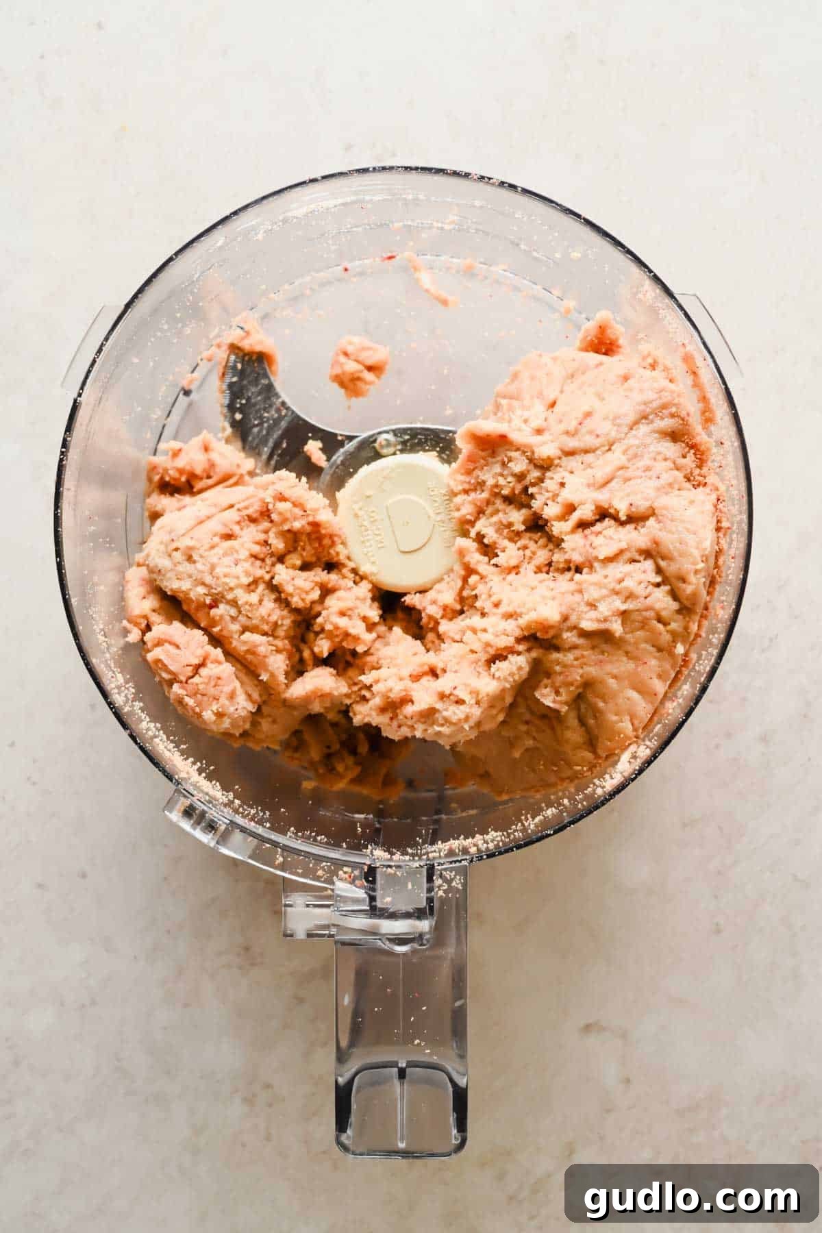A food processor containing a blended, pale pink mixture on a light countertop.