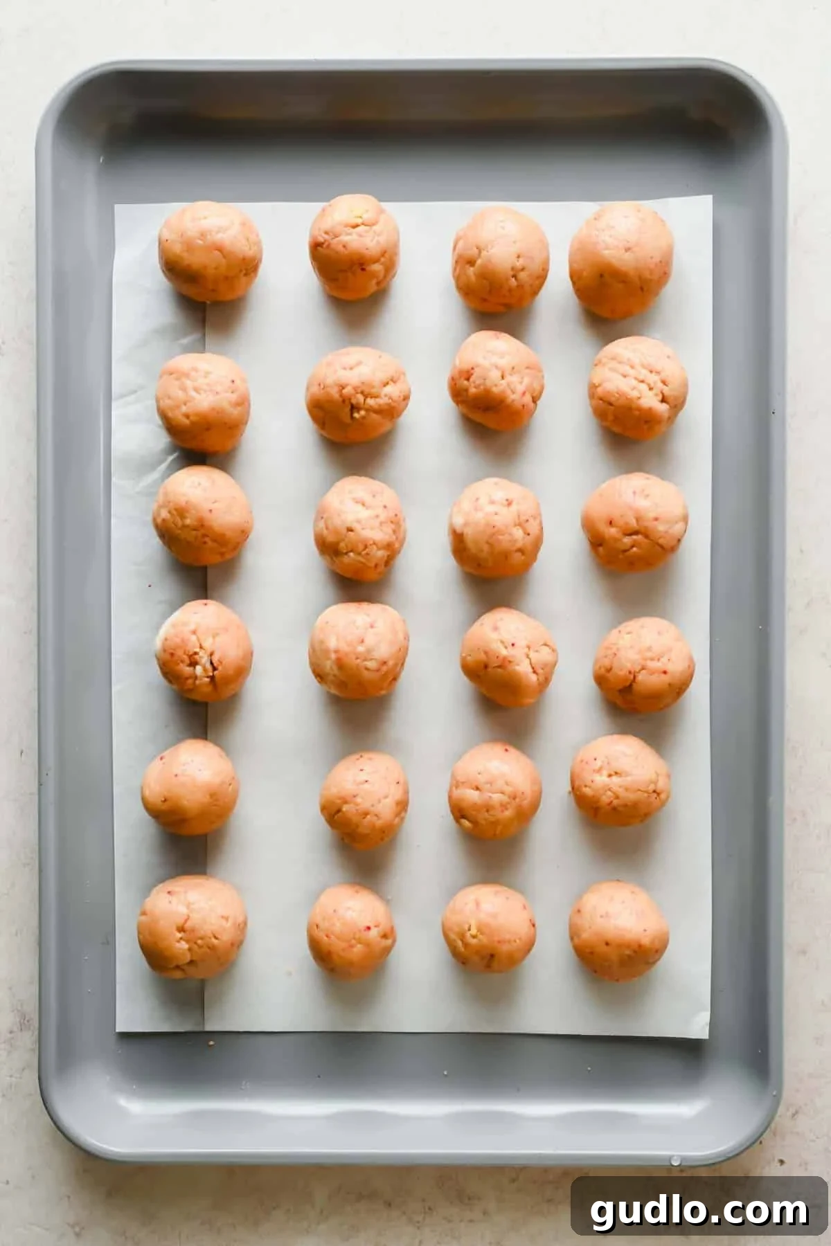 Twenty raw dough balls evenly spaced on a parchment-lined baking sheet, arranged in four rows.