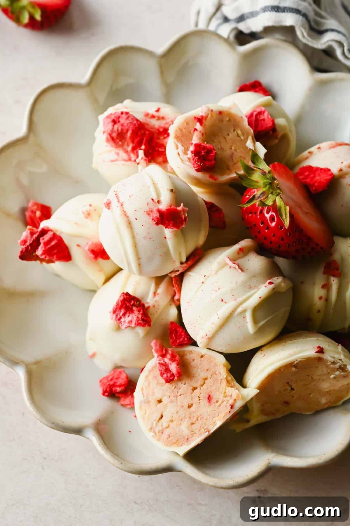 A plate of white chocolate truffles with pink strawberry pieces, some whole and some cut open to show the pink filling inside.