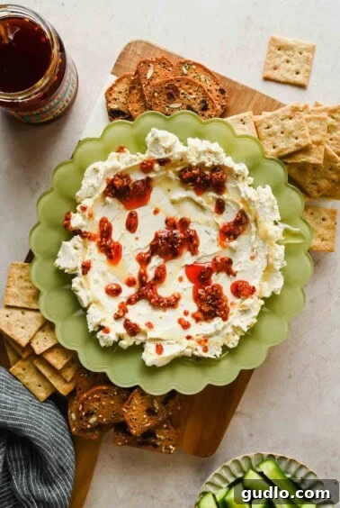 3-Ingredient Boursin Chili Crunch Dip Ready in 5 Minutes 10 Boursin chili crunch dip on a board with crackers, toast, cucumber slices, and a jar of chili crunch