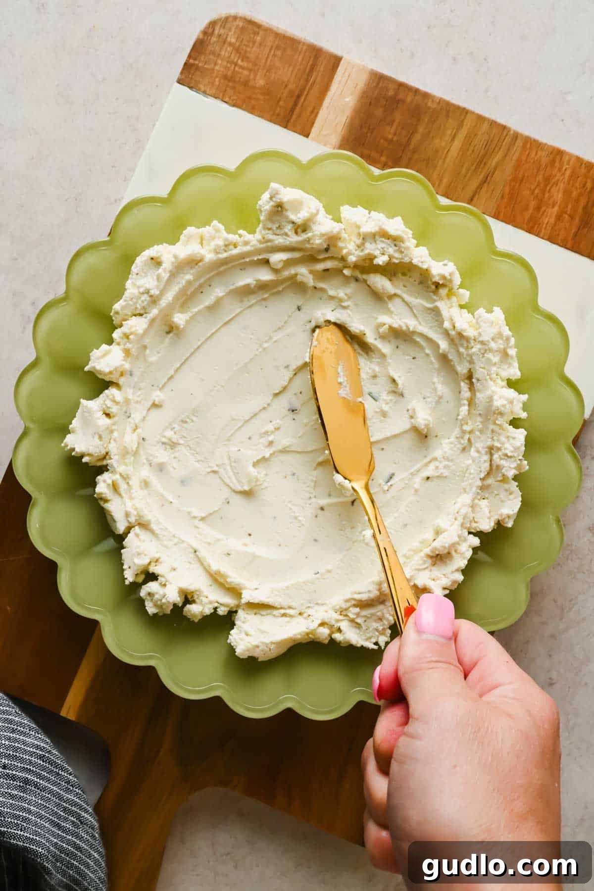 3-Ingredient Boursin Chili Crunch Dip Ready in 5 Minutes 4 Spreading Boursin cheese into a green scalloped bowl with a gold knife