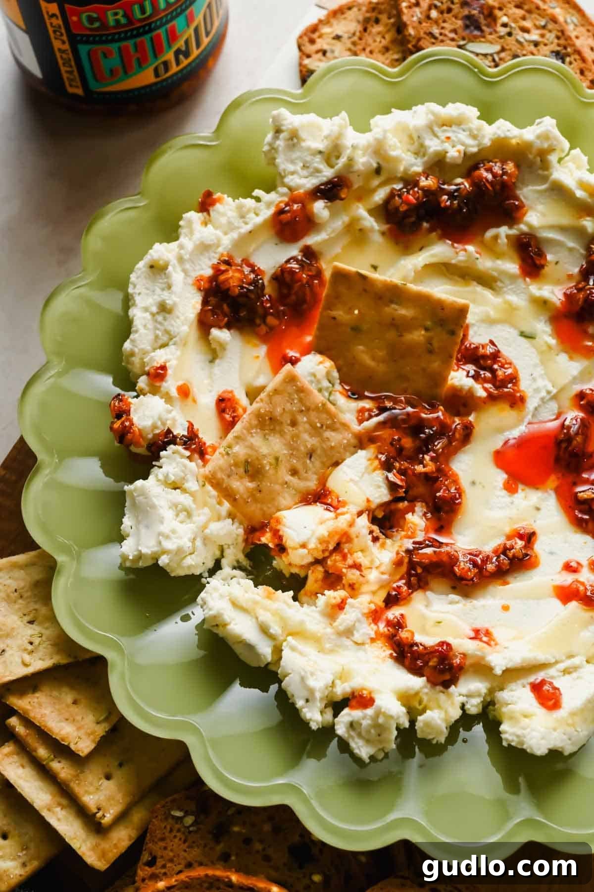 3-Ingredient Boursin Chili Crunch Dip Ready in 5 Minutes 5 Boursin cheese topped with chili crunch oil and honey in a green bowl with crackers