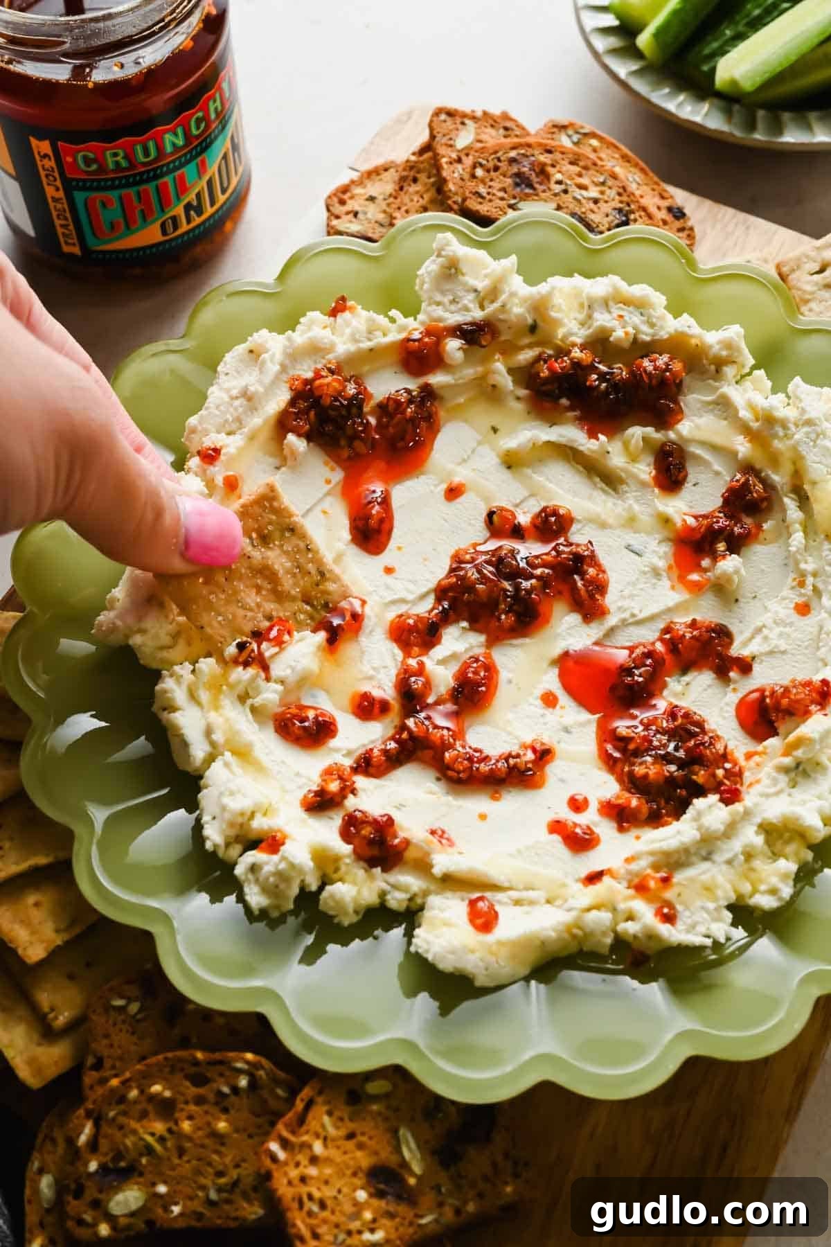 3-Ingredient Boursin Chili Crunch Dip Ready in 5 Minutes 6 A hand dipping a cracker into boursin chili crunch dip surrounded by crackers and vegetables