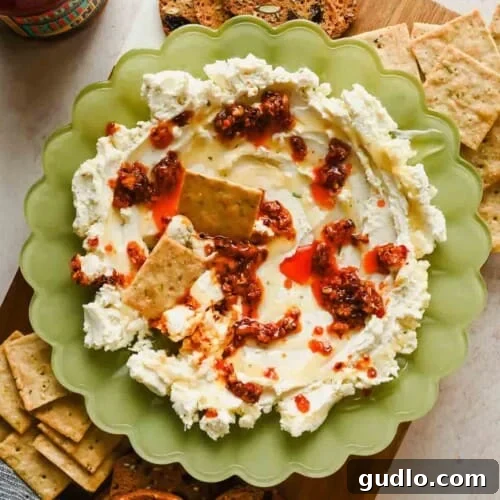 3-Ingredient Boursin Chili Crunch Dip Ready in 5 Minutes 8 Boursin chili crunch dip in a green scalloped bowl topped with chili crunch and honey, served with crackers