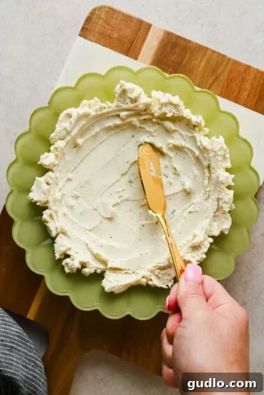 3-Ingredient Boursin Chili Crunch Dip Ready in 5 Minutes 9 Spreading Boursin cheese into a green scalloped bowl with a gold knife