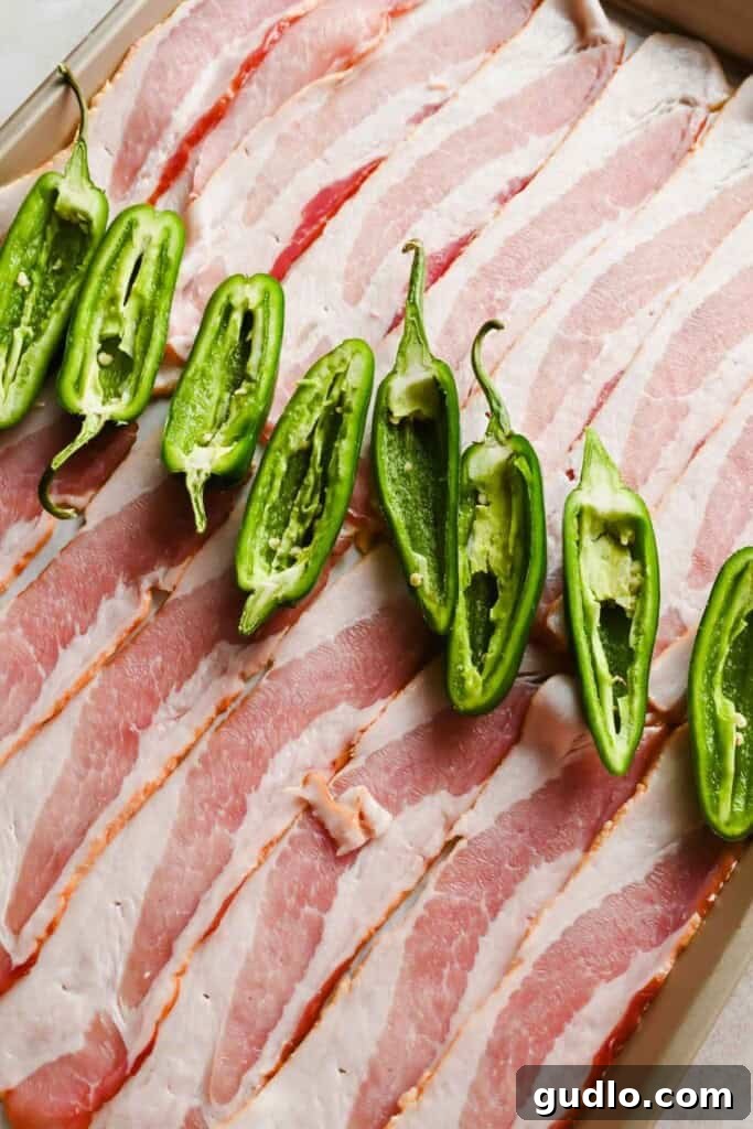 Sliced bacon and halved jalapeño peppers on a tray before roasting