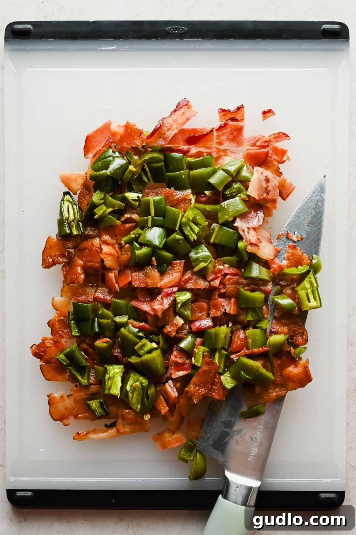 Chopped crispy bacon and roasted jalapeños on a white cutting board