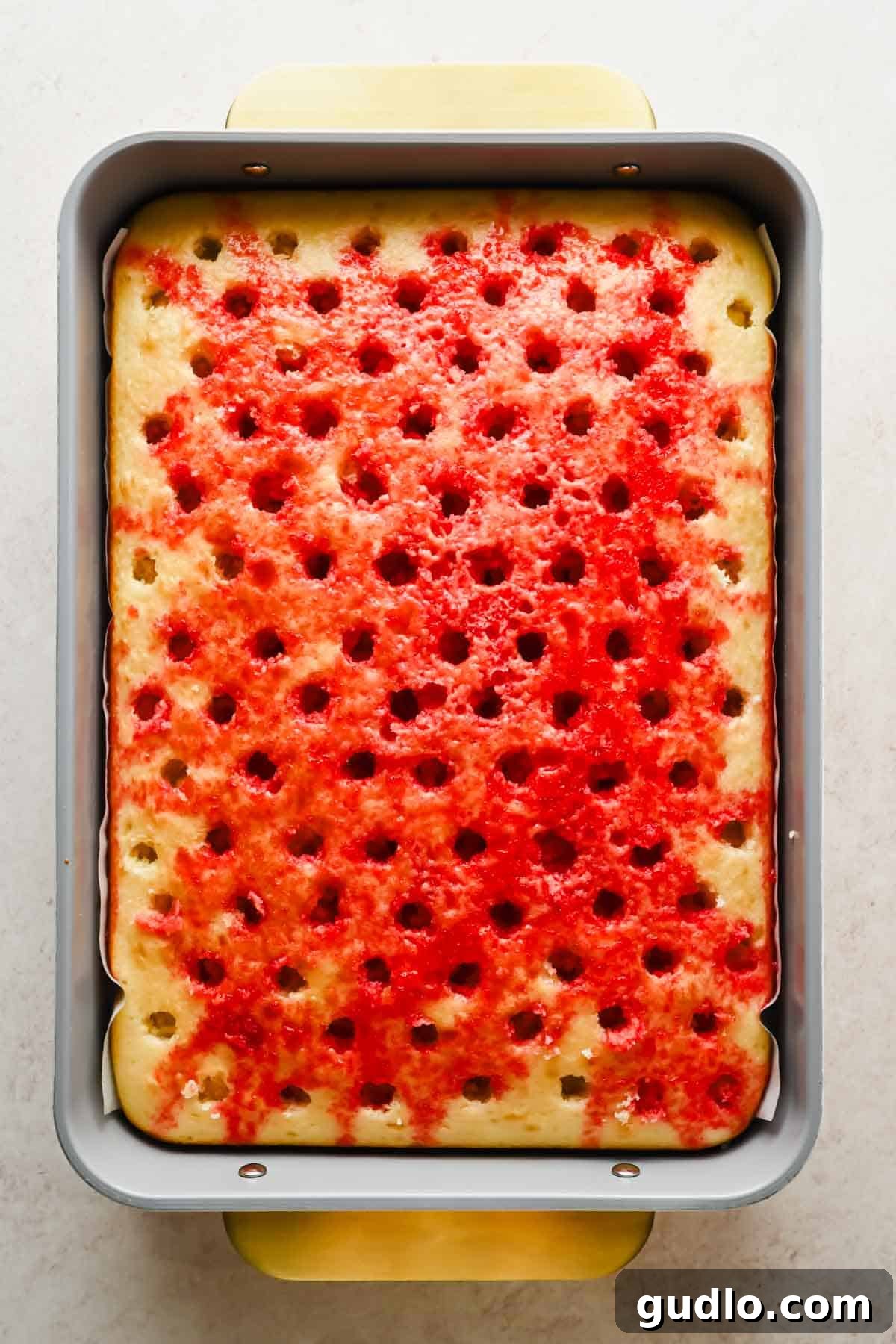 Moist Strawberry Poke Cake with Cream Cheese Frosting 5 Vanilla cake with holes filled with red strawberry Jello in a baking pan