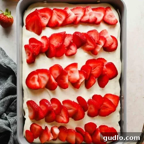 Moist Strawberry Poke Cake with Cream Cheese Frosting 9 Strawberry poke cake topped with cream cheese frosting and rows of fresh sliced strawberries in a 9x13 baking pan