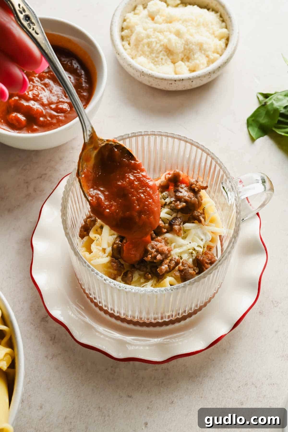 Spooning marinara sauce over lasagna layers in a mug