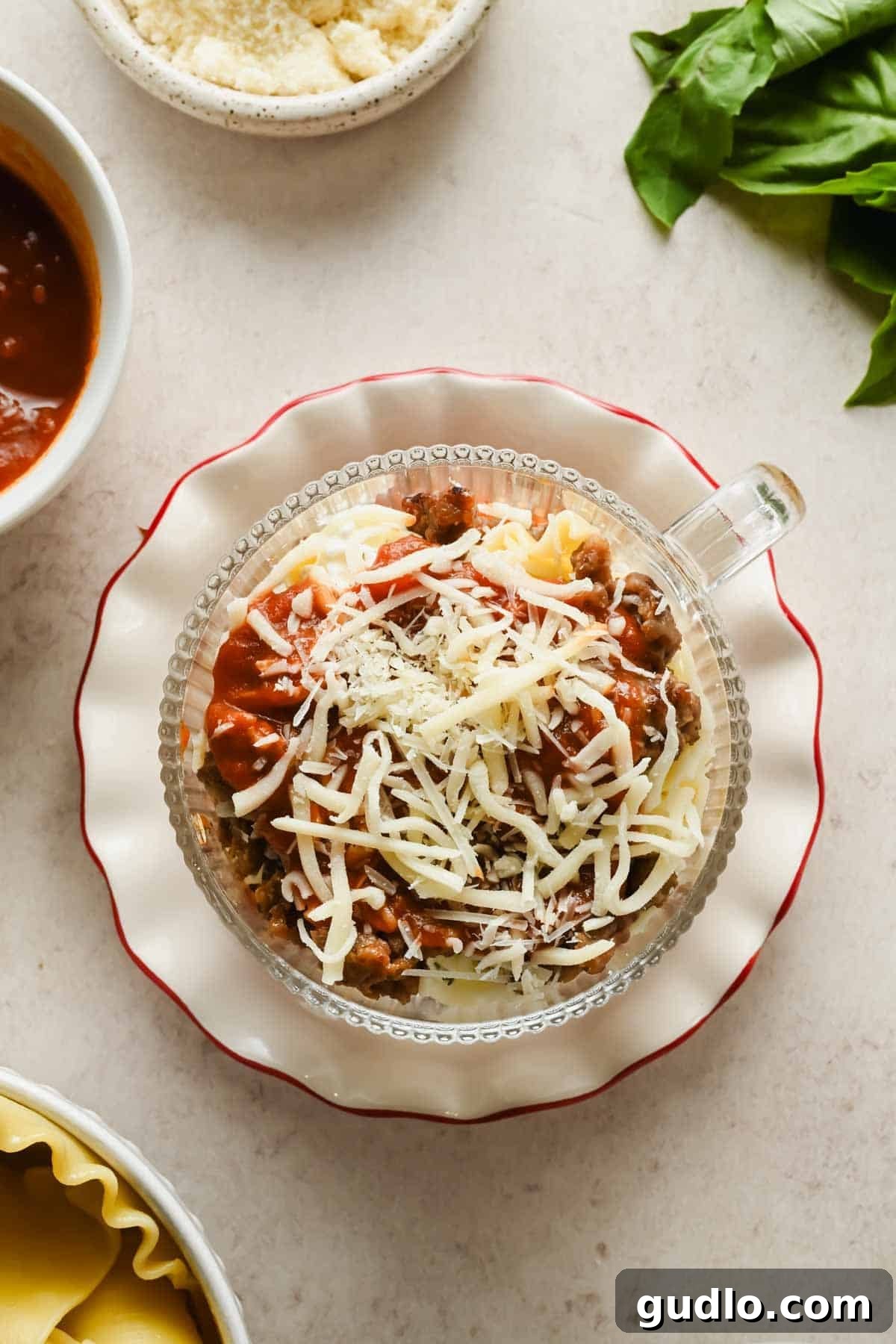 Overhead view of assembled microwave lasagna in a mug topped with shredded mozzarella