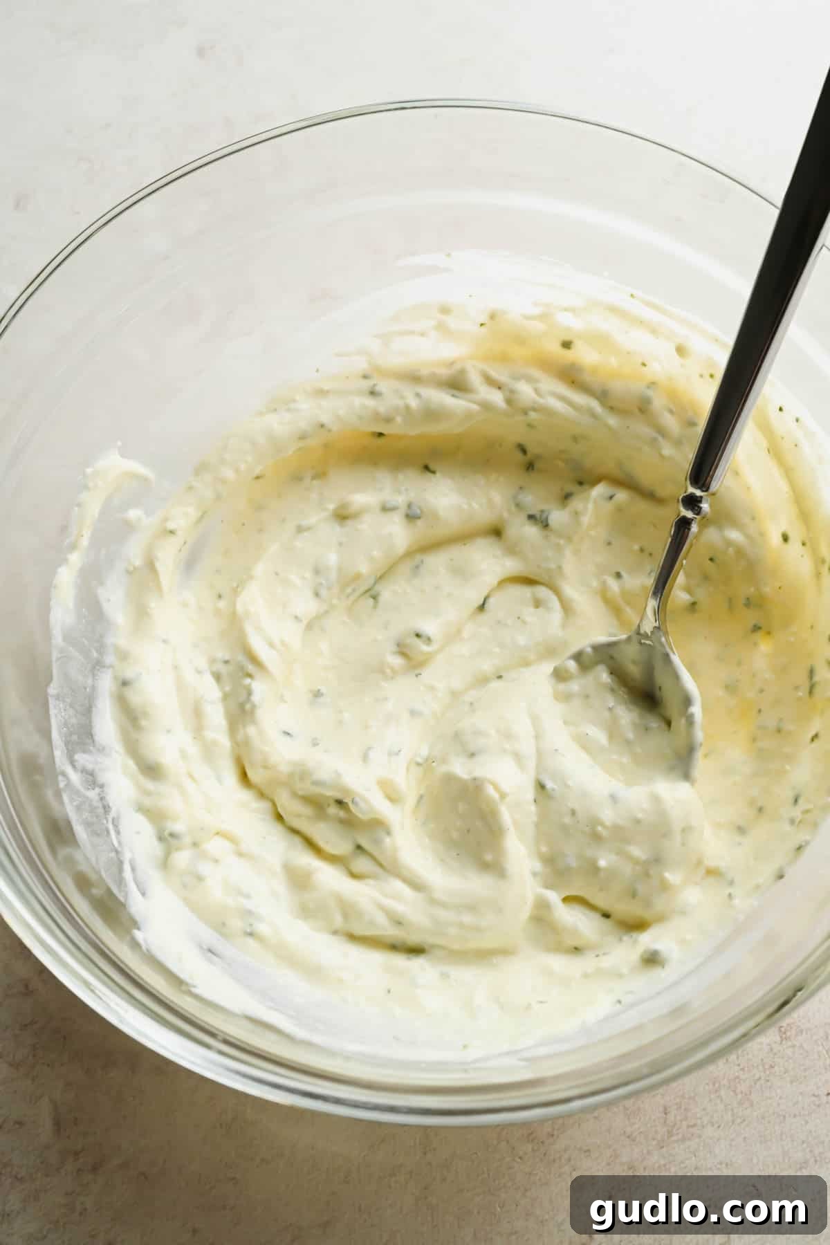 Close-up of smooth garlic and herb Boursin dressing in a glass mixing bowl.